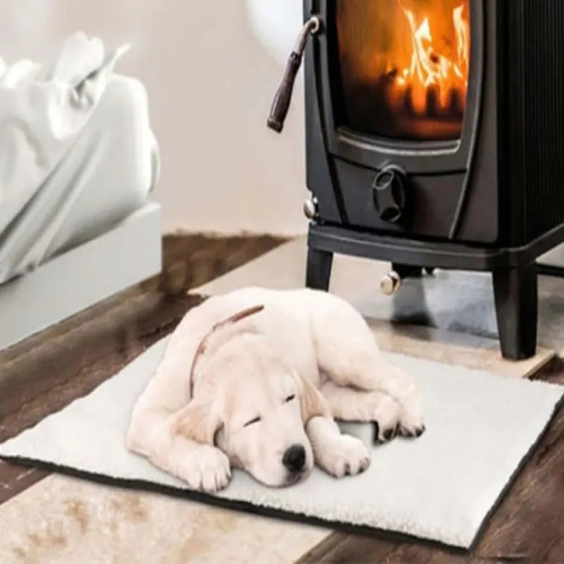A cream puppy asleep on the cream fleece self-warming mat on a wooden floor beside a wood stove