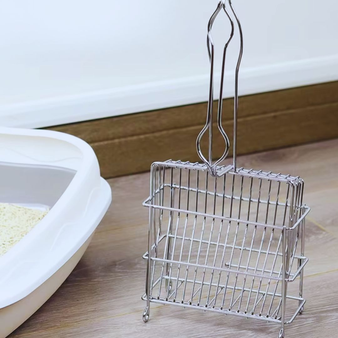 The stainless steel wire litter scoop standing upright in a wire holder beside a litter tray