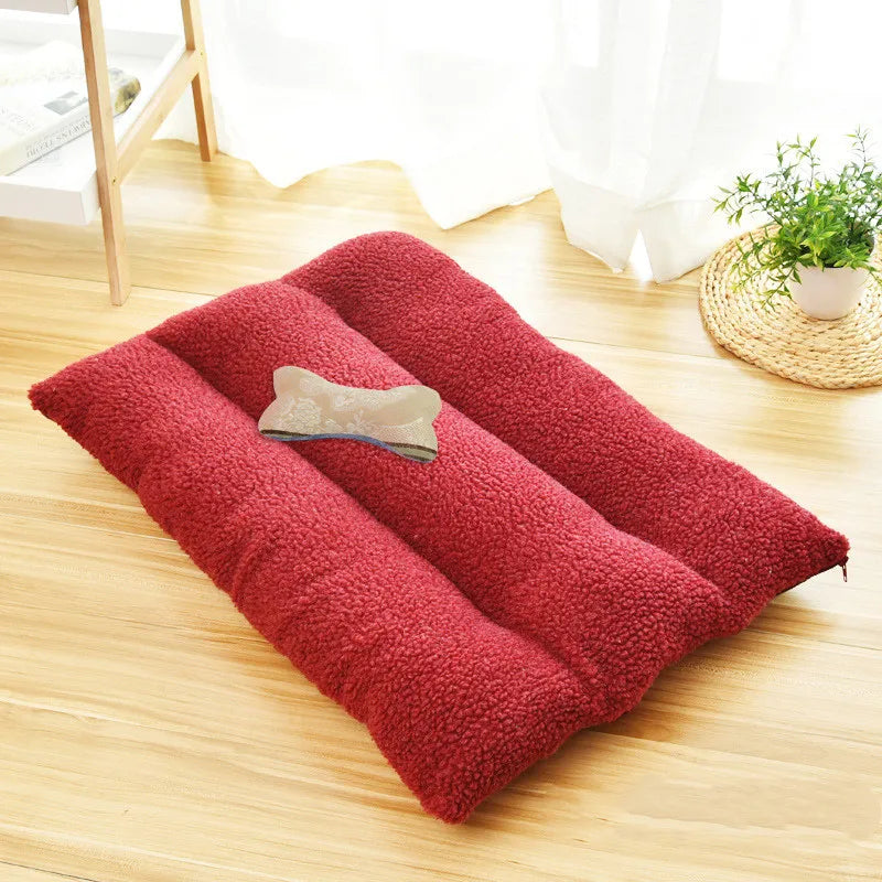 Burgundy curly-fleece dog cushion with three padded rolls on a wooden floor, a bone-shaped cushion on top