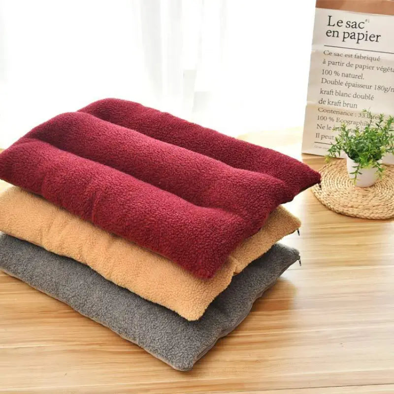 Burgundy, camel and grey curly-fleece dog cushions stacked on a wooden floor