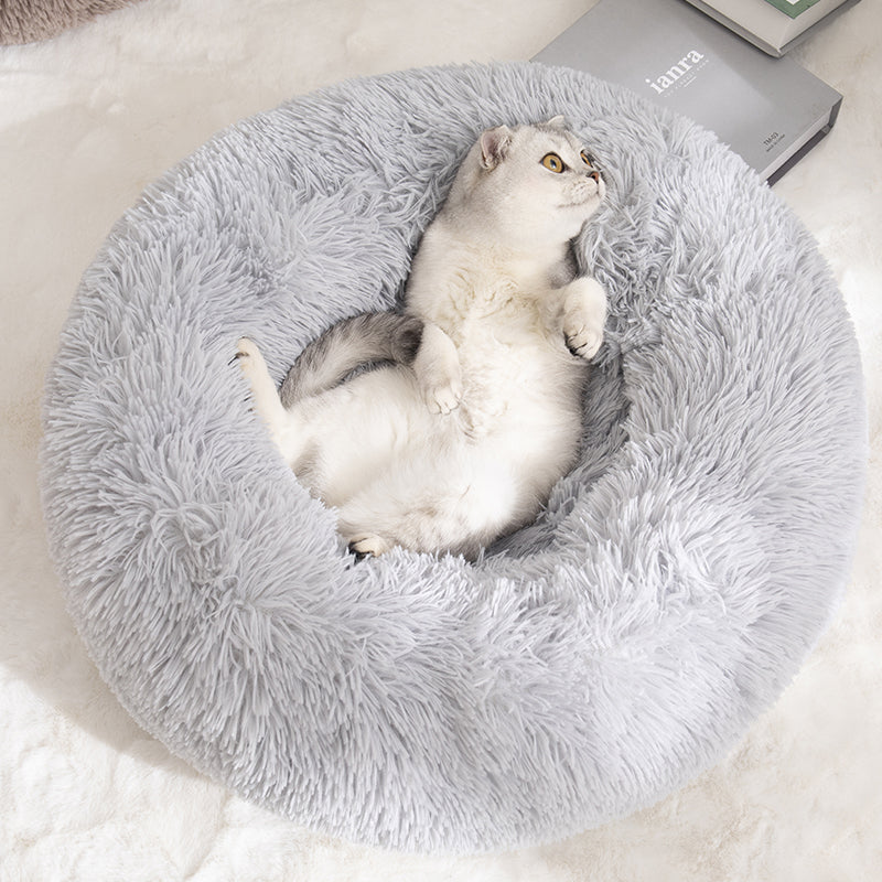 A white and grey cat lying on its back in the light grey donut bed