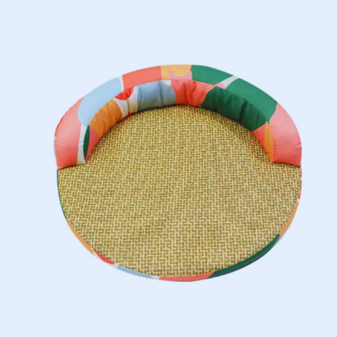 Round cat bed with a woven mat and a padded rim in a red, orange, green and pink colour block print