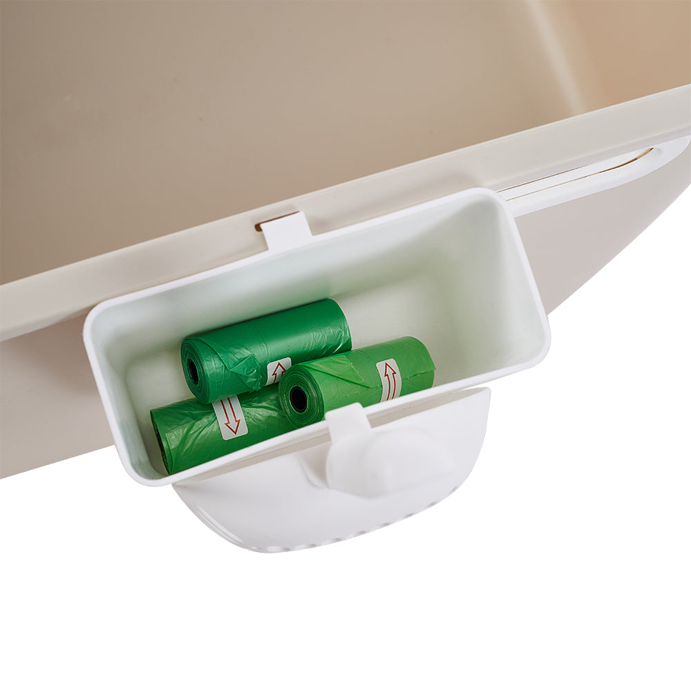 The waste bin on the rim of the litter box holding green bag rolls