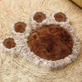 Brown paw-shaped plush pet bed mat with four toe pads and a grey-brown shaggy edge on a woven rug