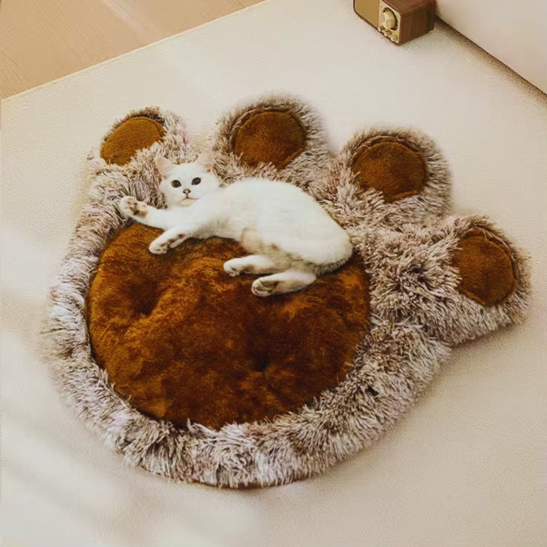 A white cat lying on the brown paw-shaped plush mat with its grey-brown shaggy edge