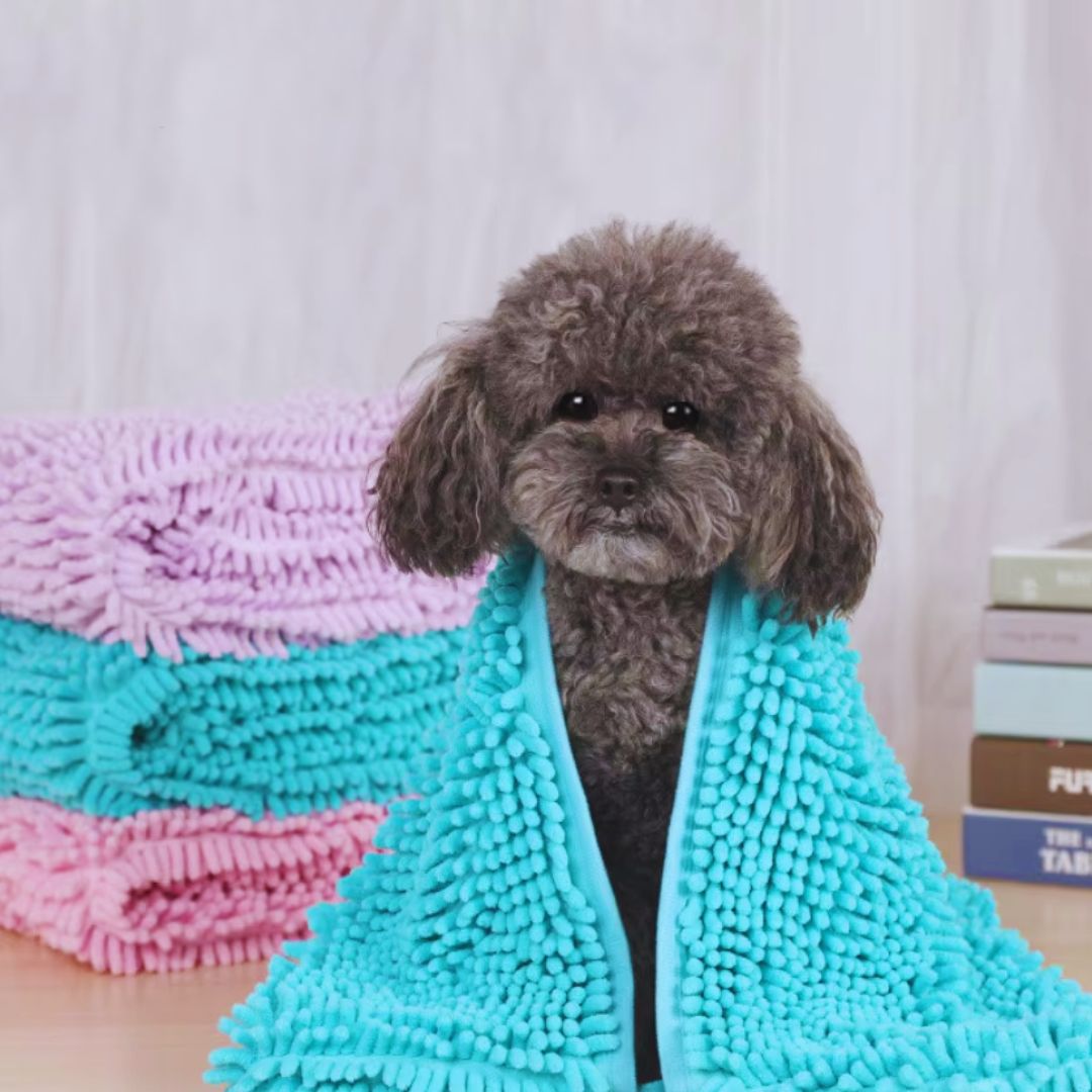 Turquoise chenille pet towel round a grey poodle, beside a stack of lilac, turquoise and pink towels
