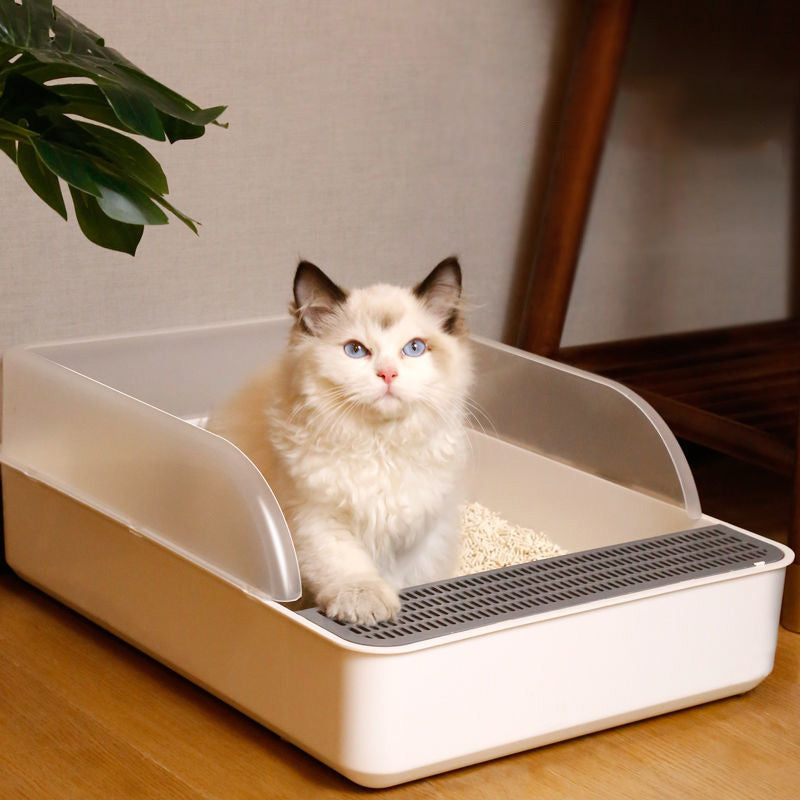 A cream cat sitting inside the open litter tray behind its clear shield