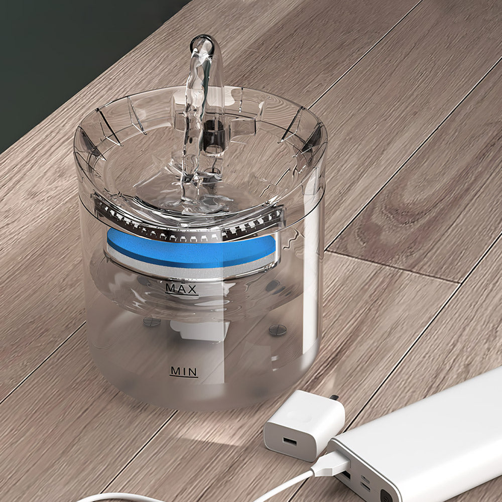 The clear water fountain with its arched spout running, the USB cable plugged into a charger beside it