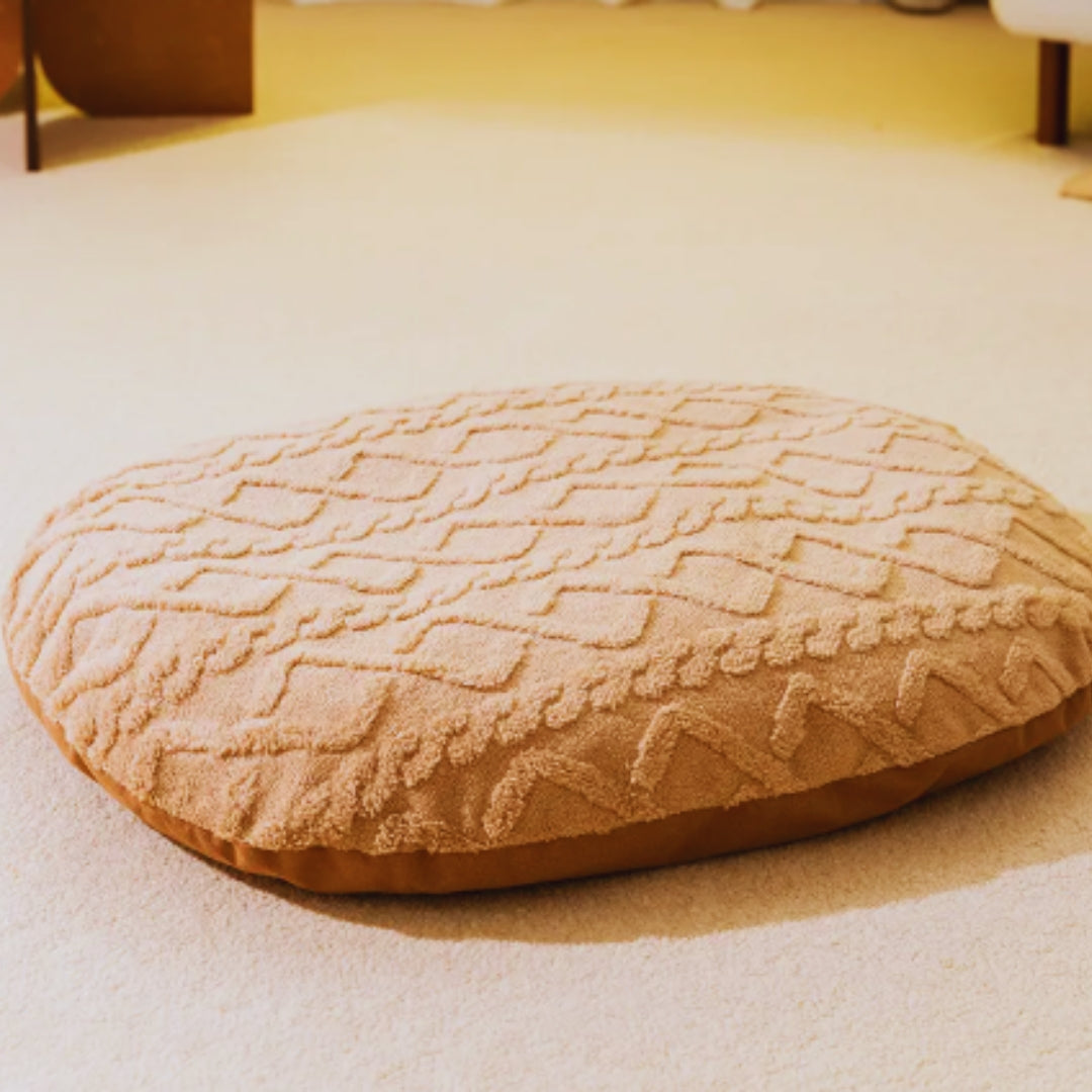 Caramel oval plush cushion on its own with a raised cable and diamond pattern