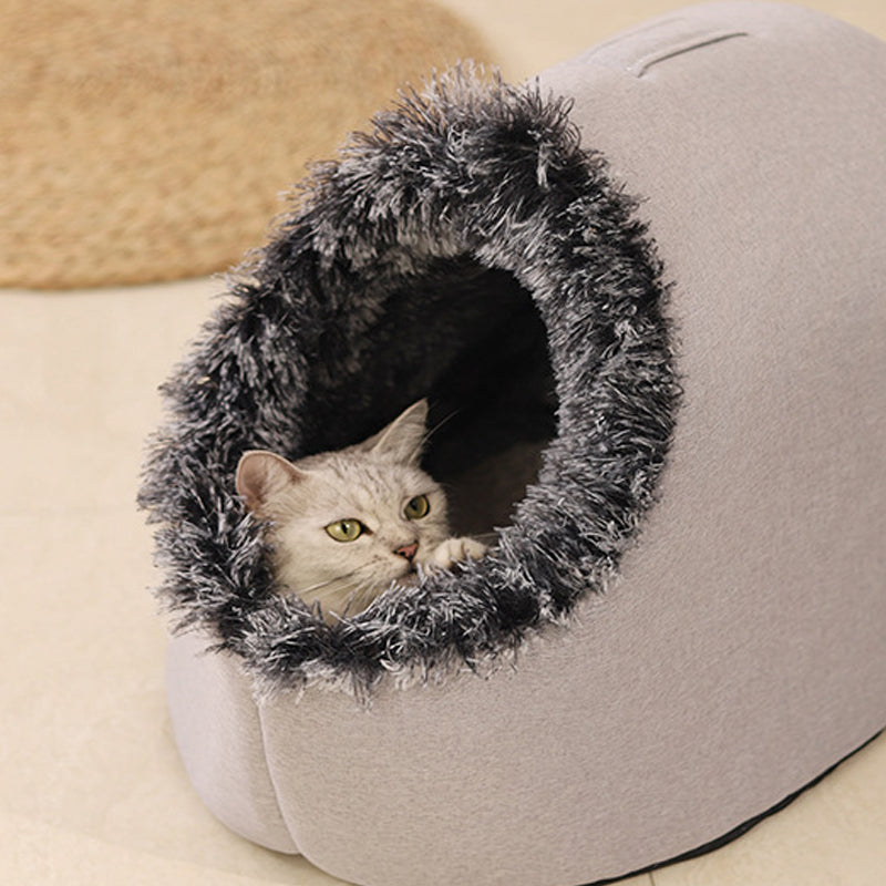 A silver tabby cat looking out of the grey cave bed with a charcoal-tipped plush entrance