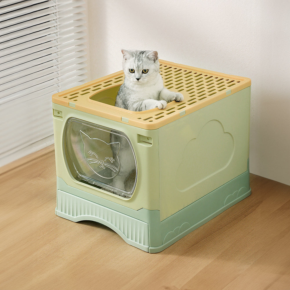 A grey tabby cat looking out of the top exit of the green enclosed litter box