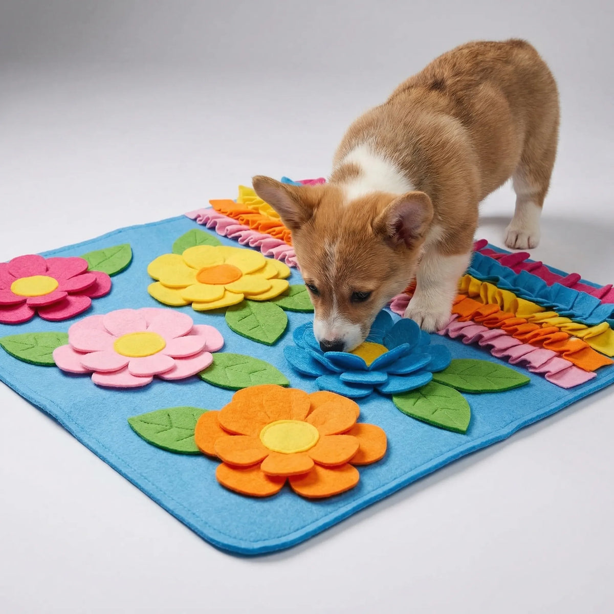 A puppy sniffing a flat blue snuffle mat with fabric flowers