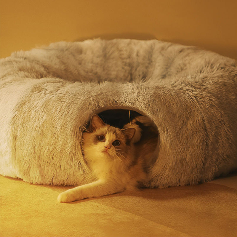 A white and ginger cat looking out of the tunnel opening of the light grey plush tunnel bed