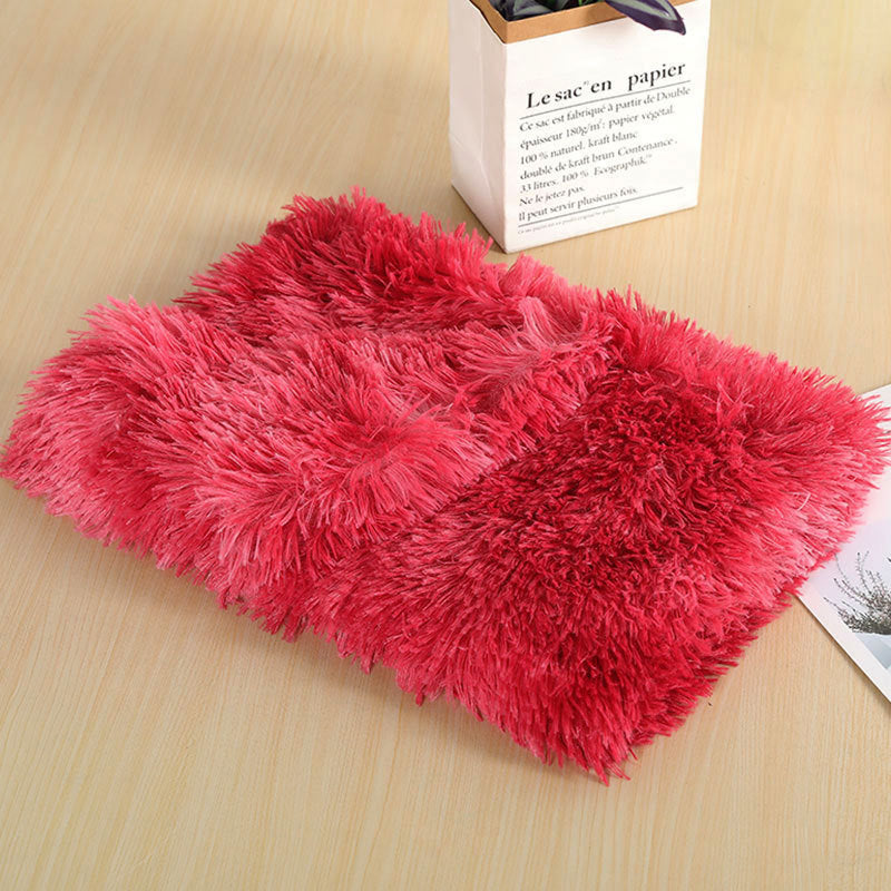 Red long-pile plush dog blanket with pink streaks, folded on a wooden table