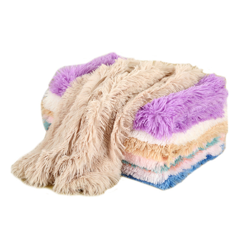 A stack of folded long-pile plush blankets with a beige one draped over the top