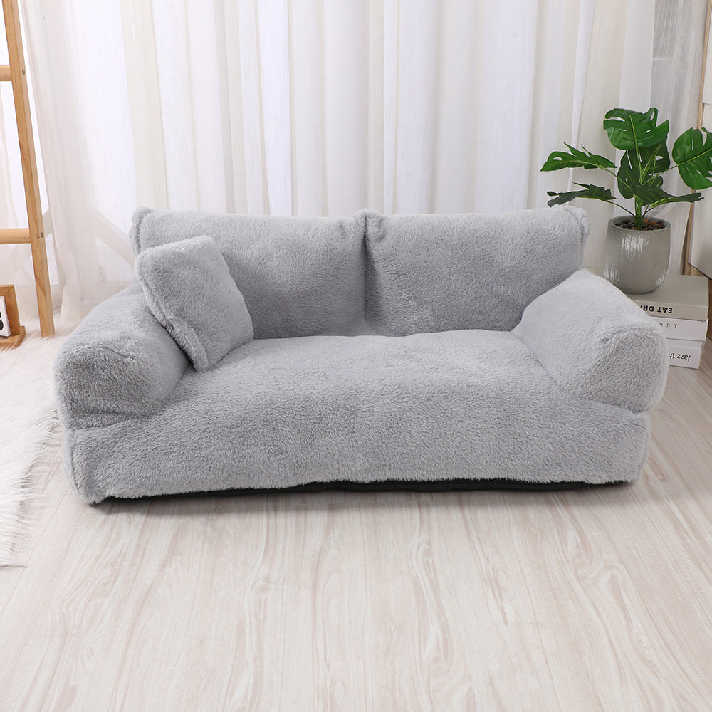 Light grey plush dog sofa bed with two armrests and a small pillow in a bright room