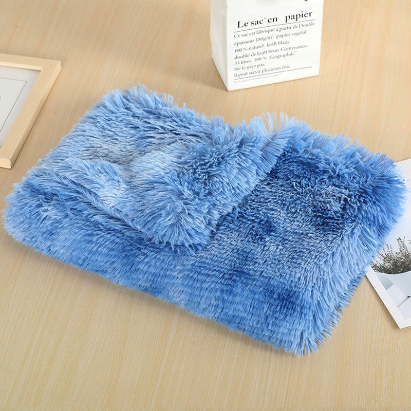 Blue long-pile plush dog blanket with lighter and darker streaks, folded on a wooden table
