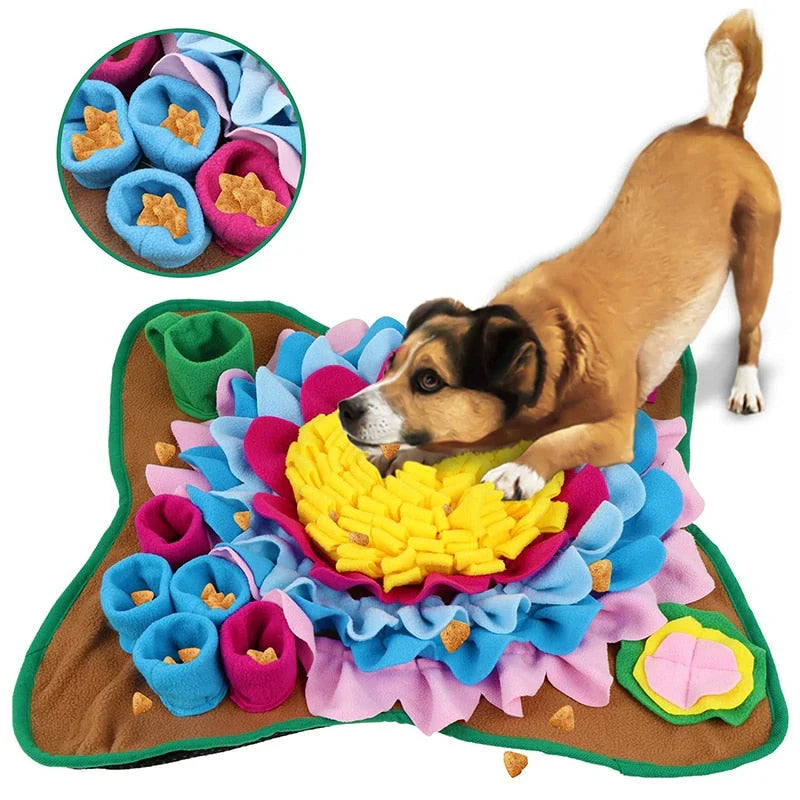 Sunflower dog snuffle mat with a yellow centre, blue and pink petals and cups, a brown and black dog searching it