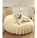 A pale puppy sitting in the cream ribbed plush donut bed