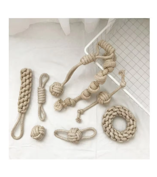Eight cotton rope dog toys laid out on a white cloth beside a white wire rack