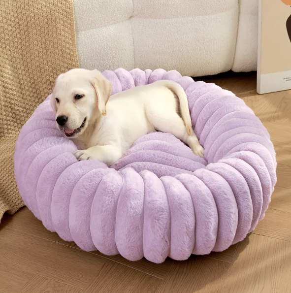 A pale puppy lying in the lilac ribbed plush donut bed