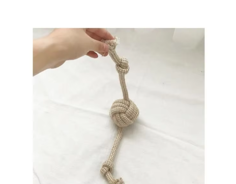 Cotton rope dog toy with a ball in the middle and knotted, frayed ends, held up by one end