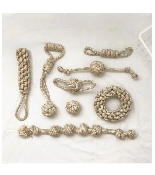 Eight cotton rope dog toys laid out on white: braided stick, ball with handle, coiled double loop, rope with ball, ball with two loops, rope ball, braided ring and knotted rope