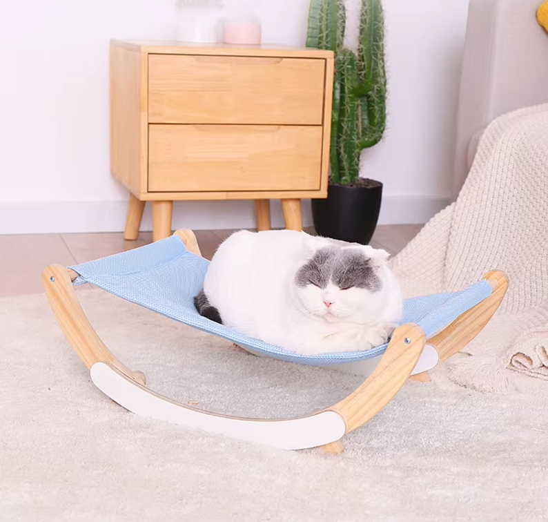 A grey and white cat curled up in the blue sling of the wooden rocking cat hammock in a bedroom