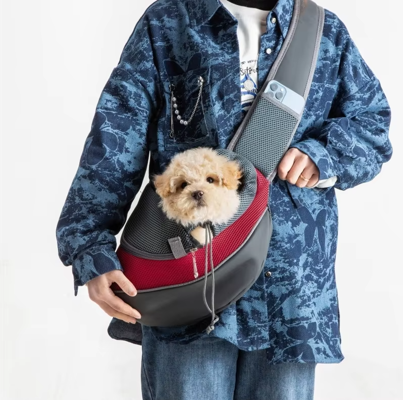 A small curly dog looking out of the red mesh pet sling worn across a person's body