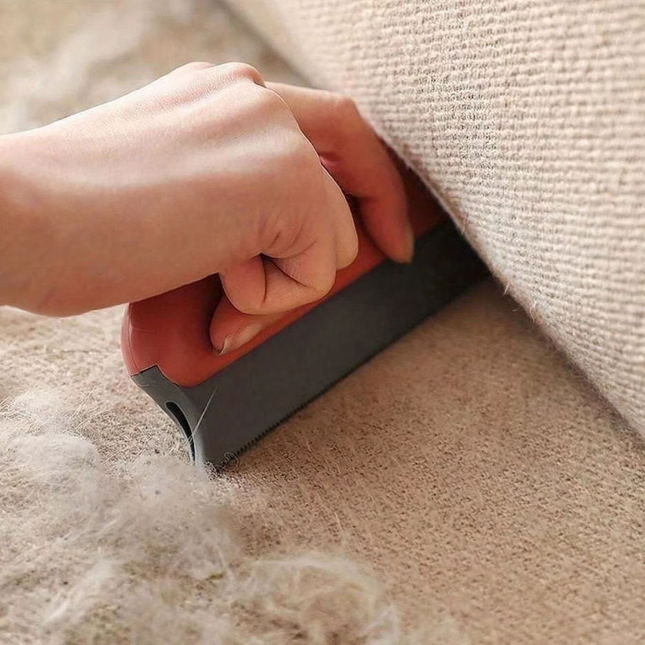 A coral pet hair remover lifting hair off a beige carpet beside a sofa