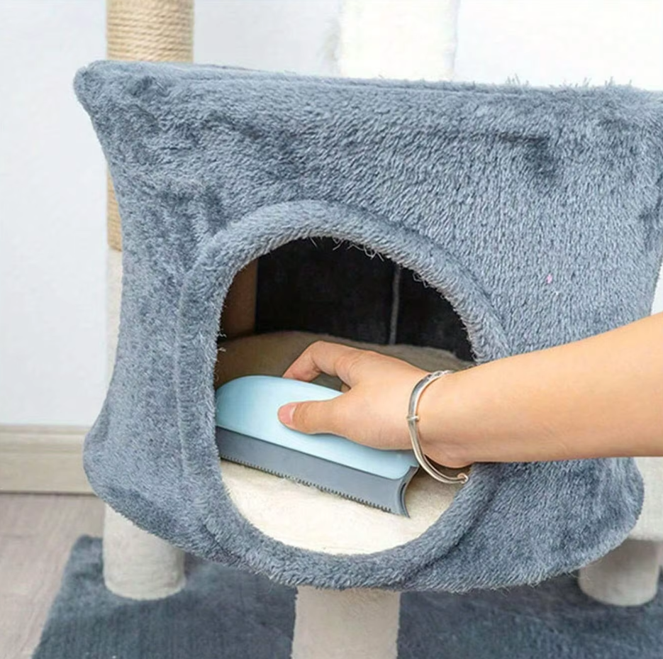 A hand using the light blue pet hair remover inside the plush hideaway of a cat tree