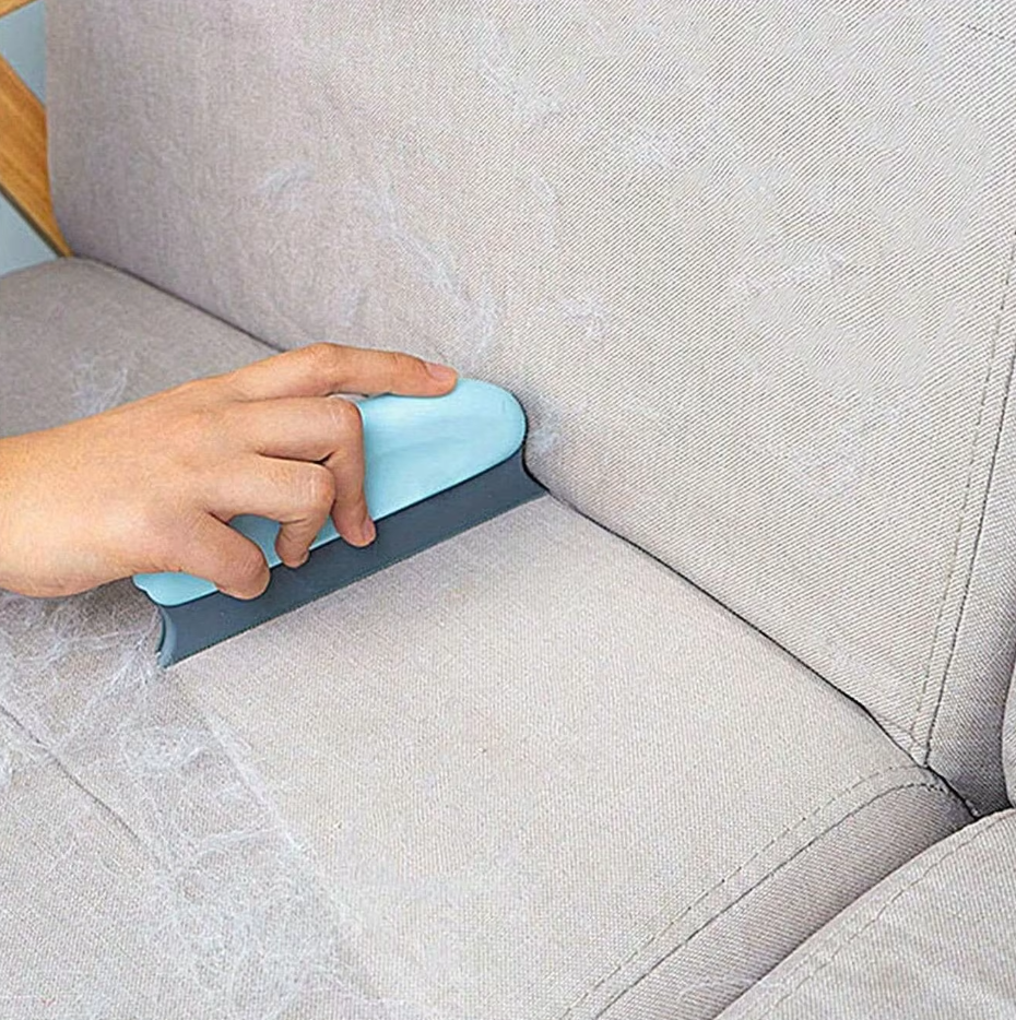 The light blue pet hair remover reaching into the seam between a sofa seat and its back