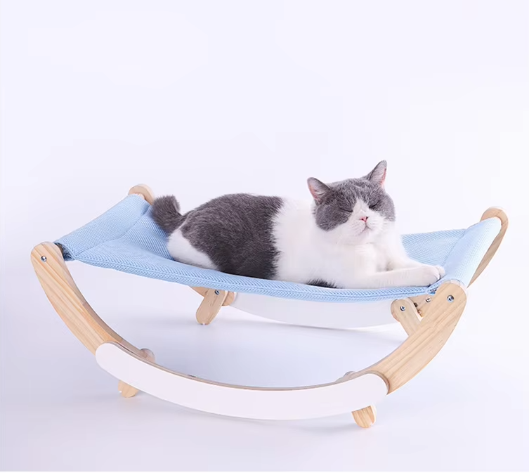 A grey and white cat lying in the blue sling of the rocking cat hammock, seen from the side