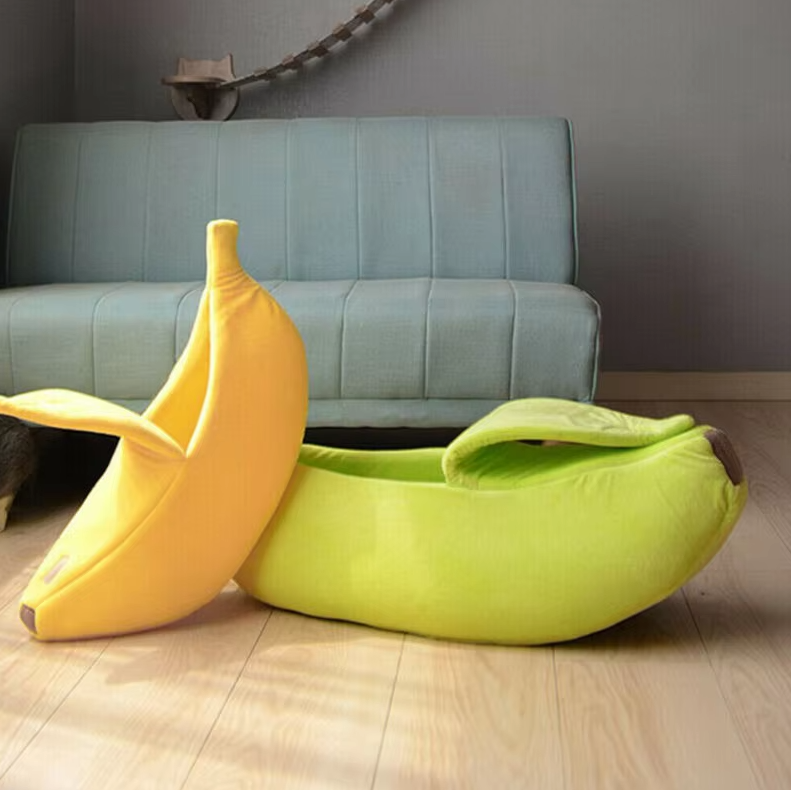 A green banana cat bed on a wooden floor beside a yellow one standing on its end