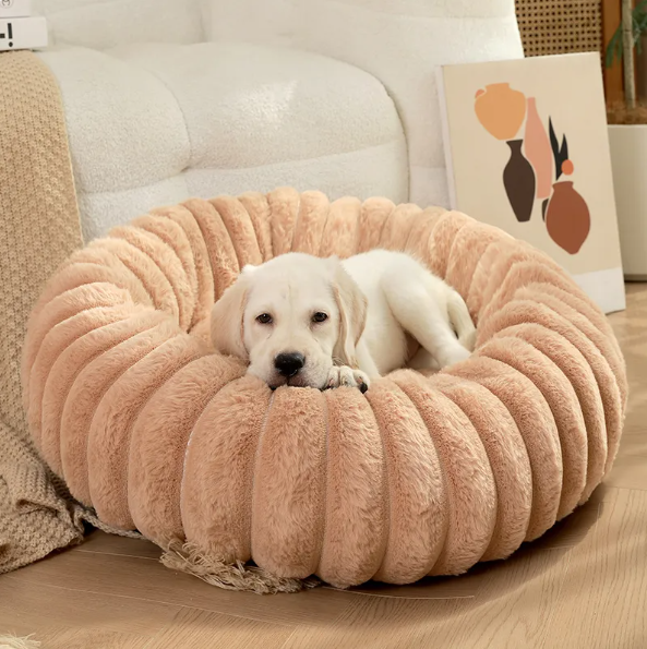A pale puppy resting its head on the rim of the caramel ribbed plush donut bed
