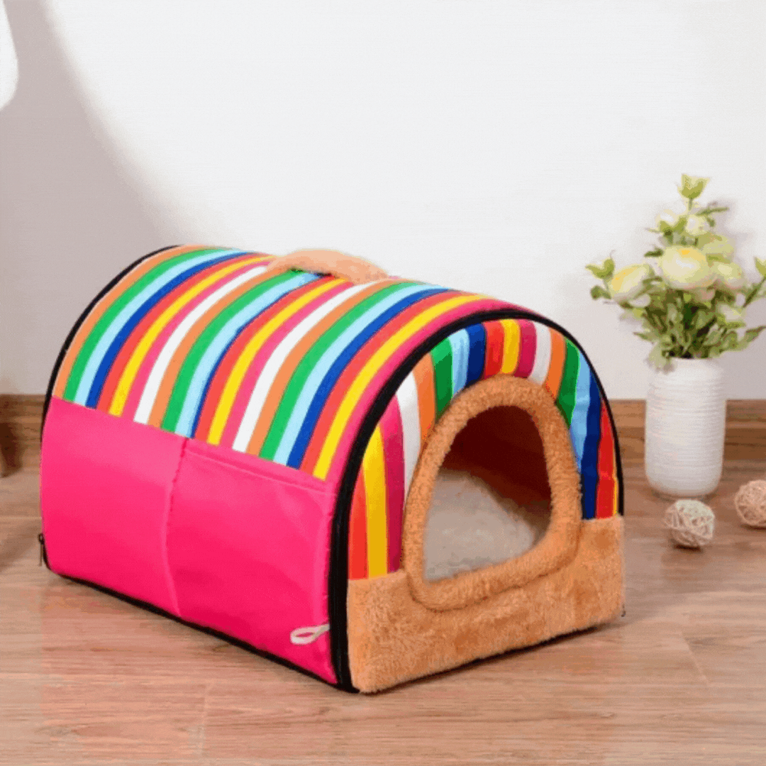 Rainbow-striped tunnel pet house with pink sides and a tan plush doorway on a wooden floor