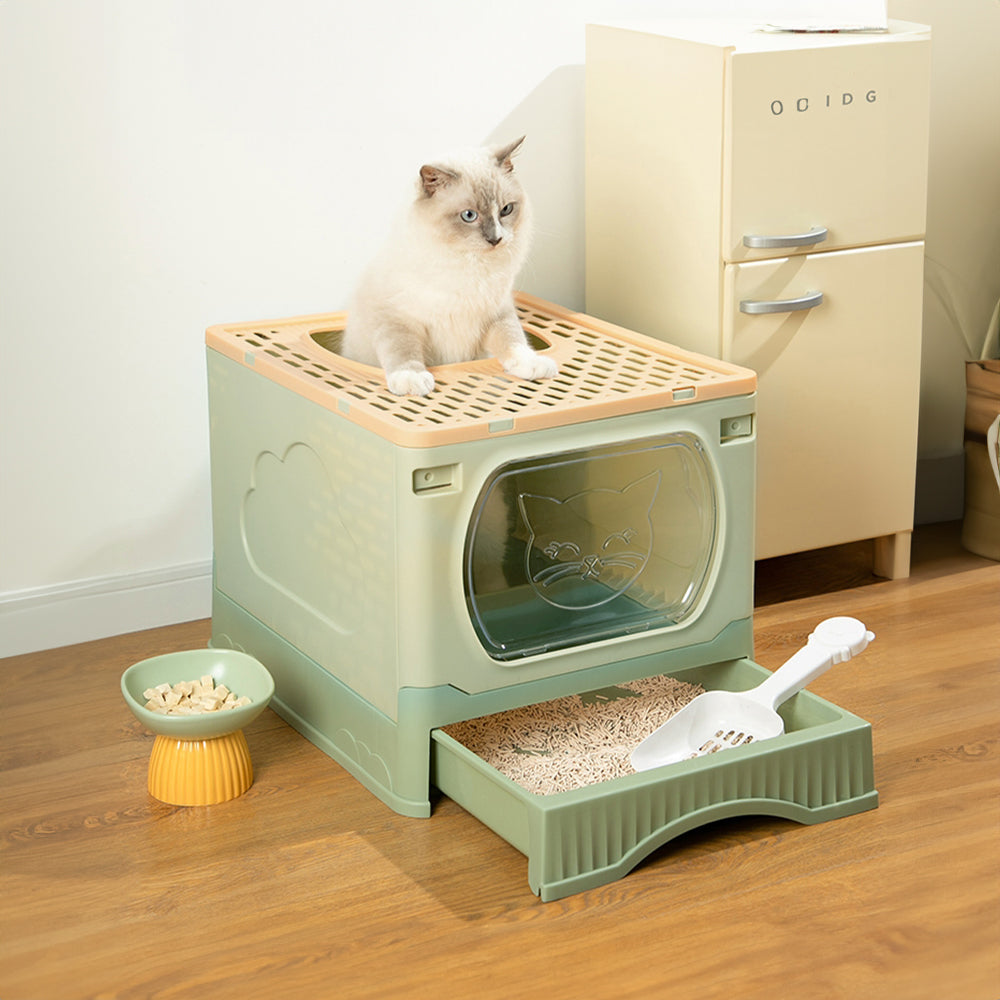 A white cat on top of the litter box with its drawer pulled out and a scoop