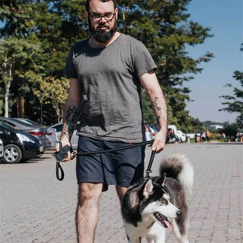 A man walking a husky on the black bungee lead, holding the padded end handle