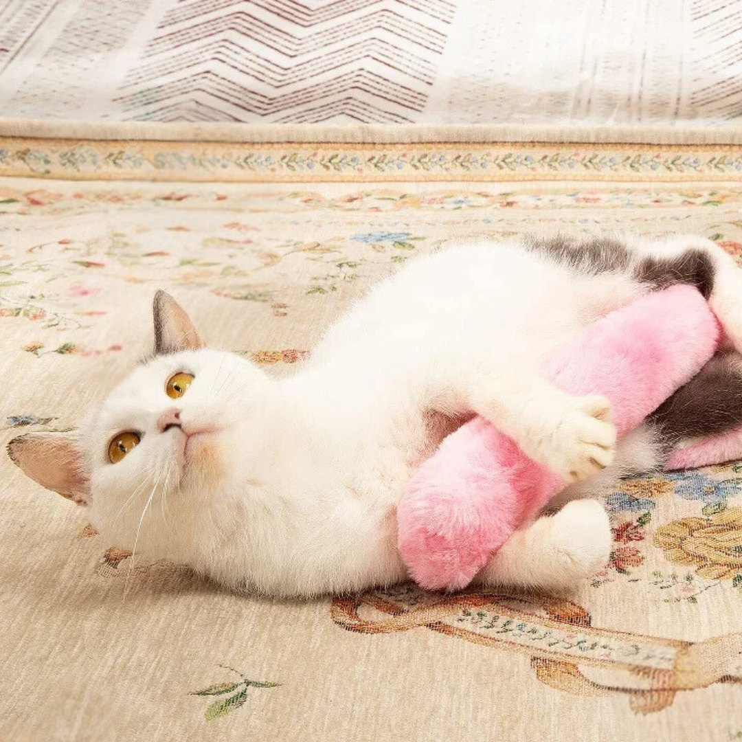A white cat lying on its back hugging the pink tie-dye catnip kicker pillow