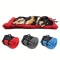 A dog asleep on the red travel bed, with the bed rolled up in red, grey and blue