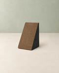 Small triangular cat scratcher with a brown corrugated cardboard face and black sides, on a cream floor against a pale sage wall
