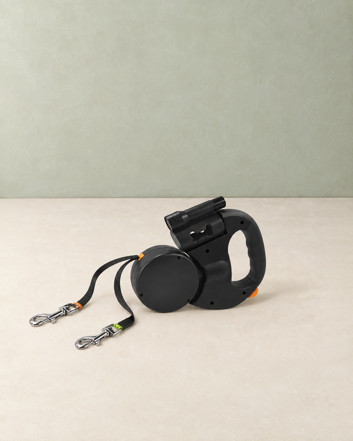 Black retractable double dog lead lying on a cream floor, its two tapes and metal clips pulled out