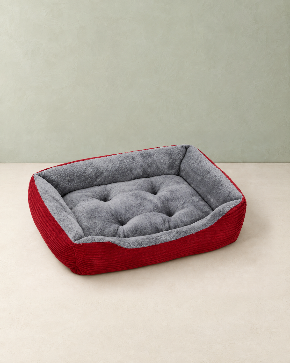 Red rectangular dog bed with raised ribbed sides and a tufted grey plush seat, on a cream floor against a pale sage wall