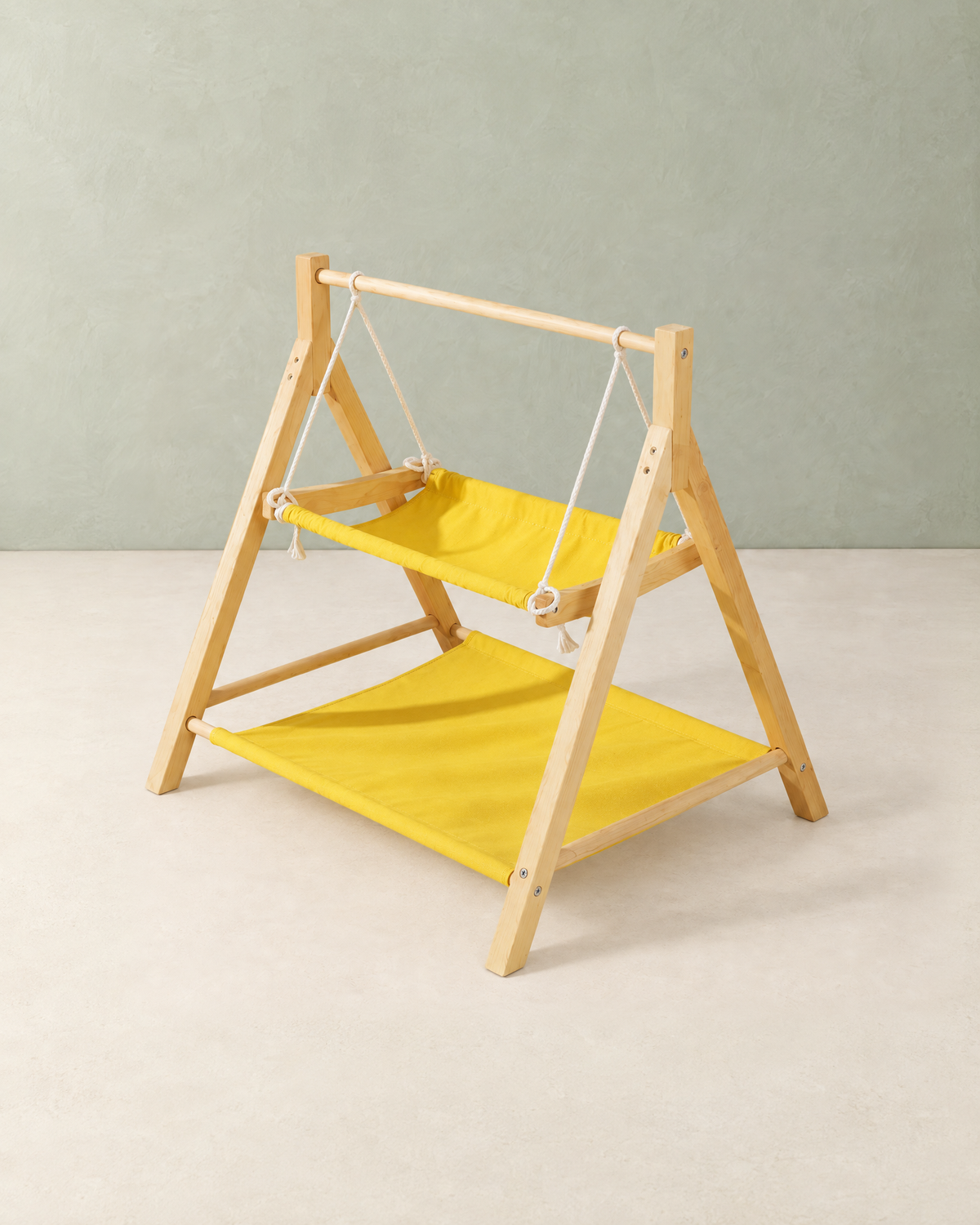 Wooden cat swing bed with a yellow swing hammock on white ropes and a yellow hammock below, on a cream floor against a pale sage wall
