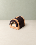 Dark brown tunnel-shaped pet house with tan plush trim and a plush-framed doorway, on a cream floor against a pale sage wall