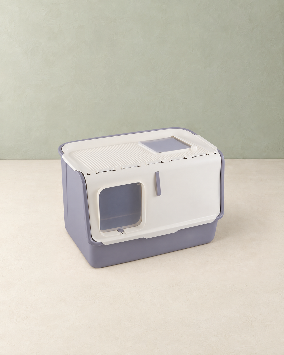 White and grey hooded cat litter box with a front flap door and a ridged top with a flap, on a cream floor against a pale sage wall