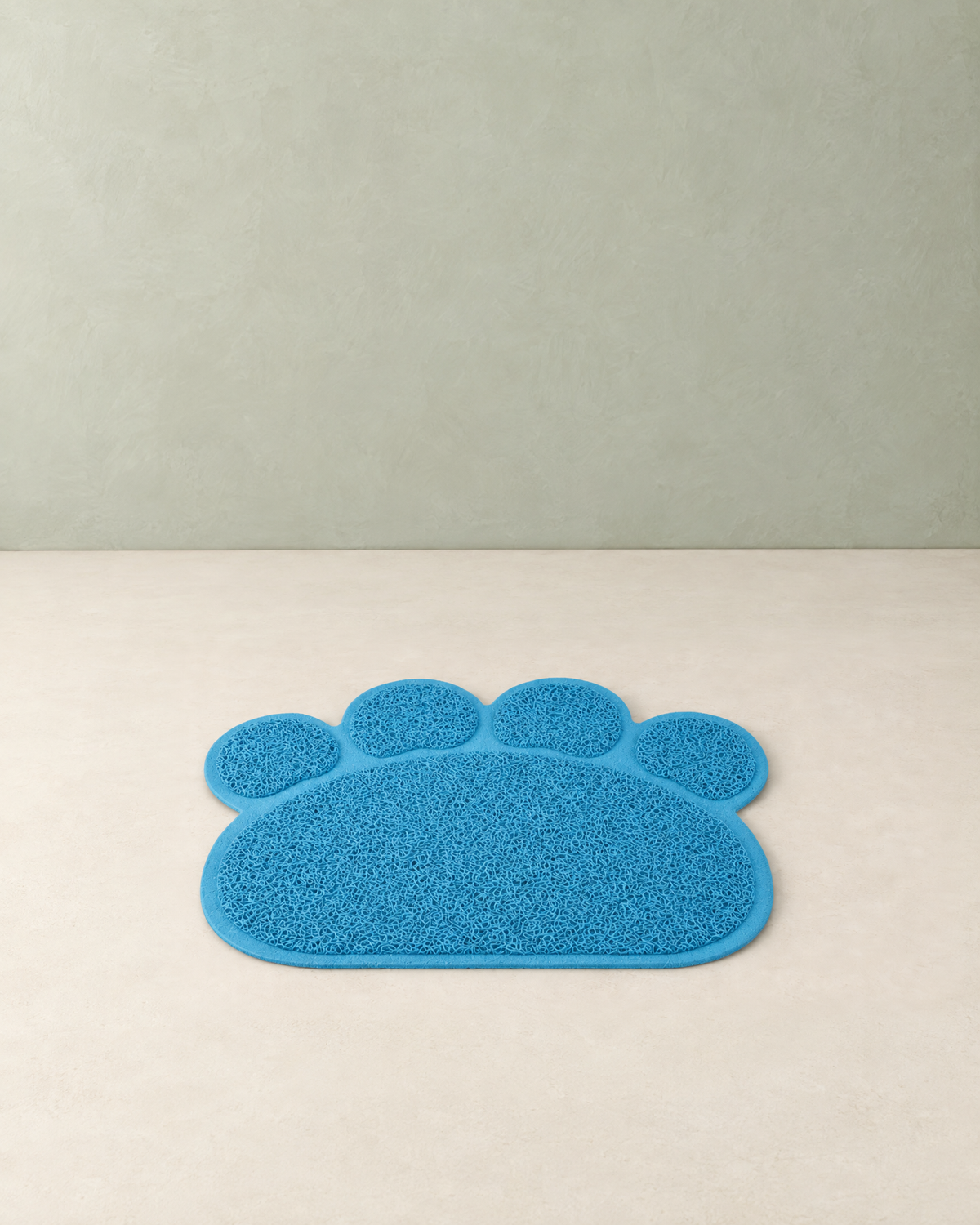 Sky blue paw-shaped cat litter mat with four toe pads lying flat on a cream floor against a pale sage wall