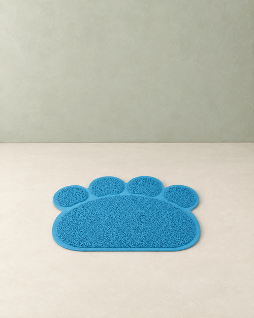 Sky blue paw-shaped cat litter mat with four toe pads lying flat on a cream floor against a pale sage wall