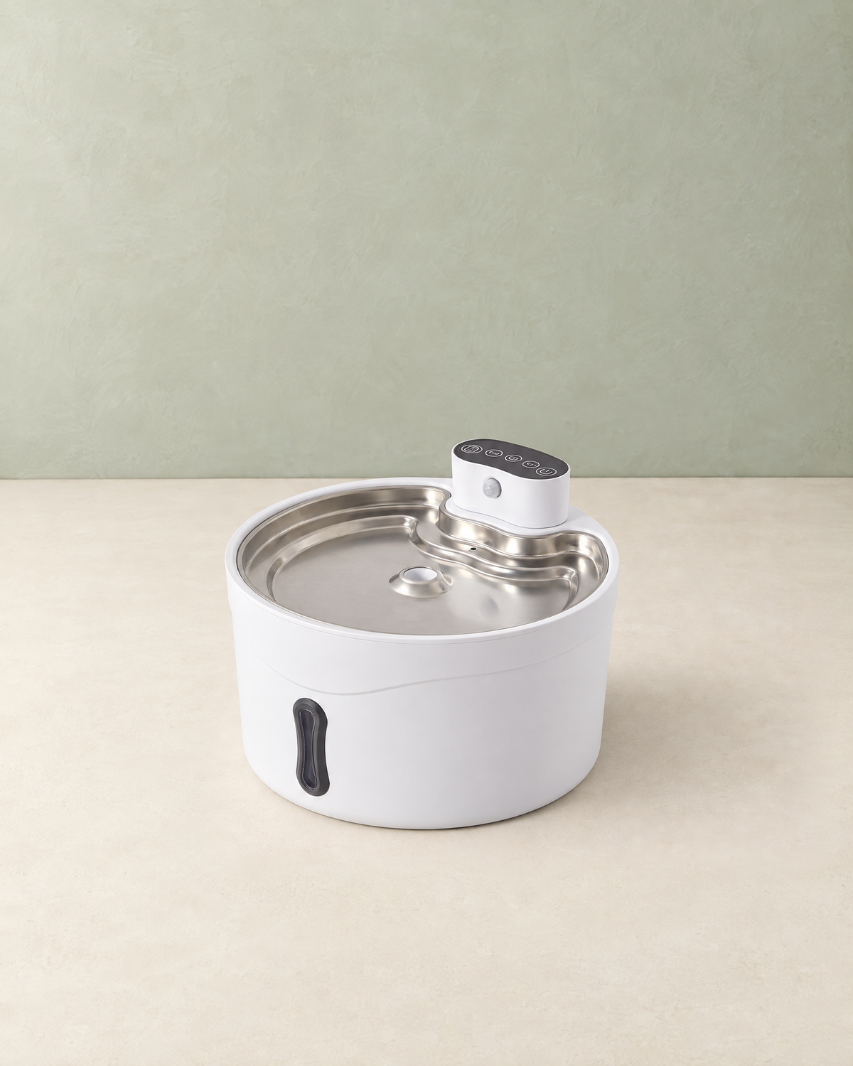 White round pet water fountain with a stainless steel tray and a control module on top, on a cream floor against a pale sage wall