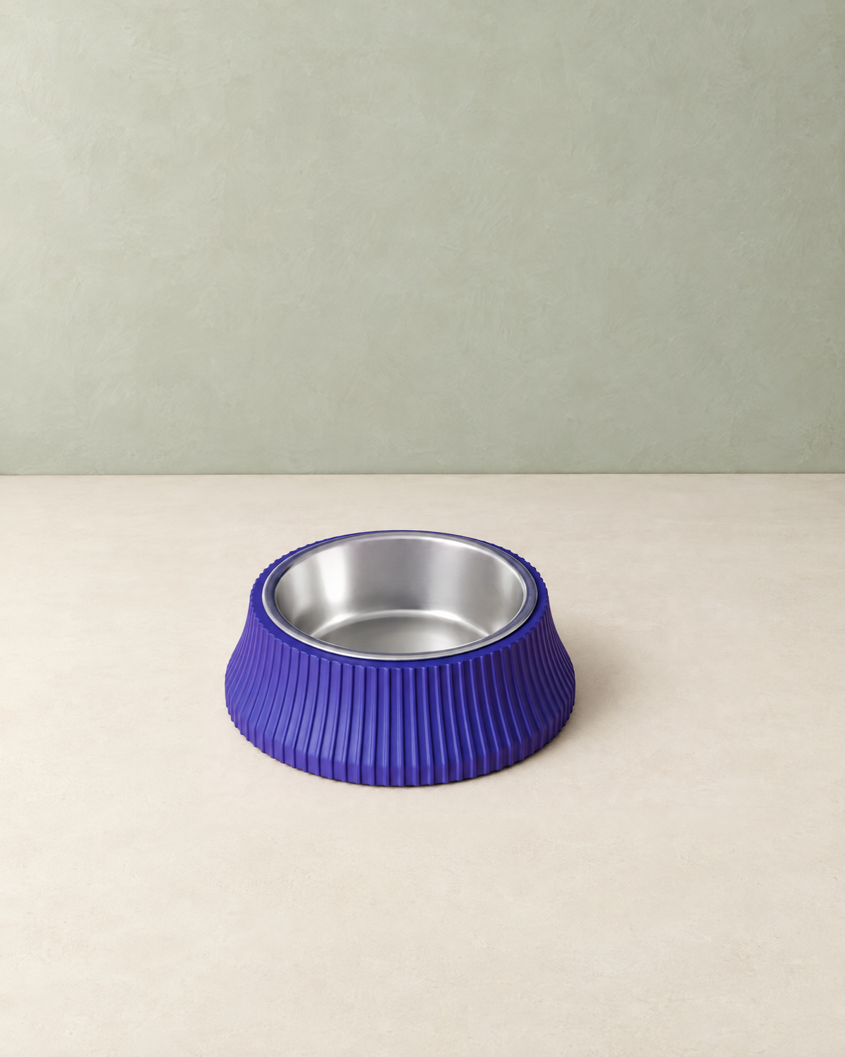 Round violet-blue ribbed dog bowl with a stainless steel insert on a cream floor against a pale sage wall